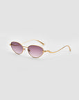 For Art's Sake® Rebirth sunglasses feature gold oval frames, purple-tinted lenses, and subtly wavy arms, merging classic elegance with a modern twist. Presented on a light gray background, they capture the spirit of innovative style.