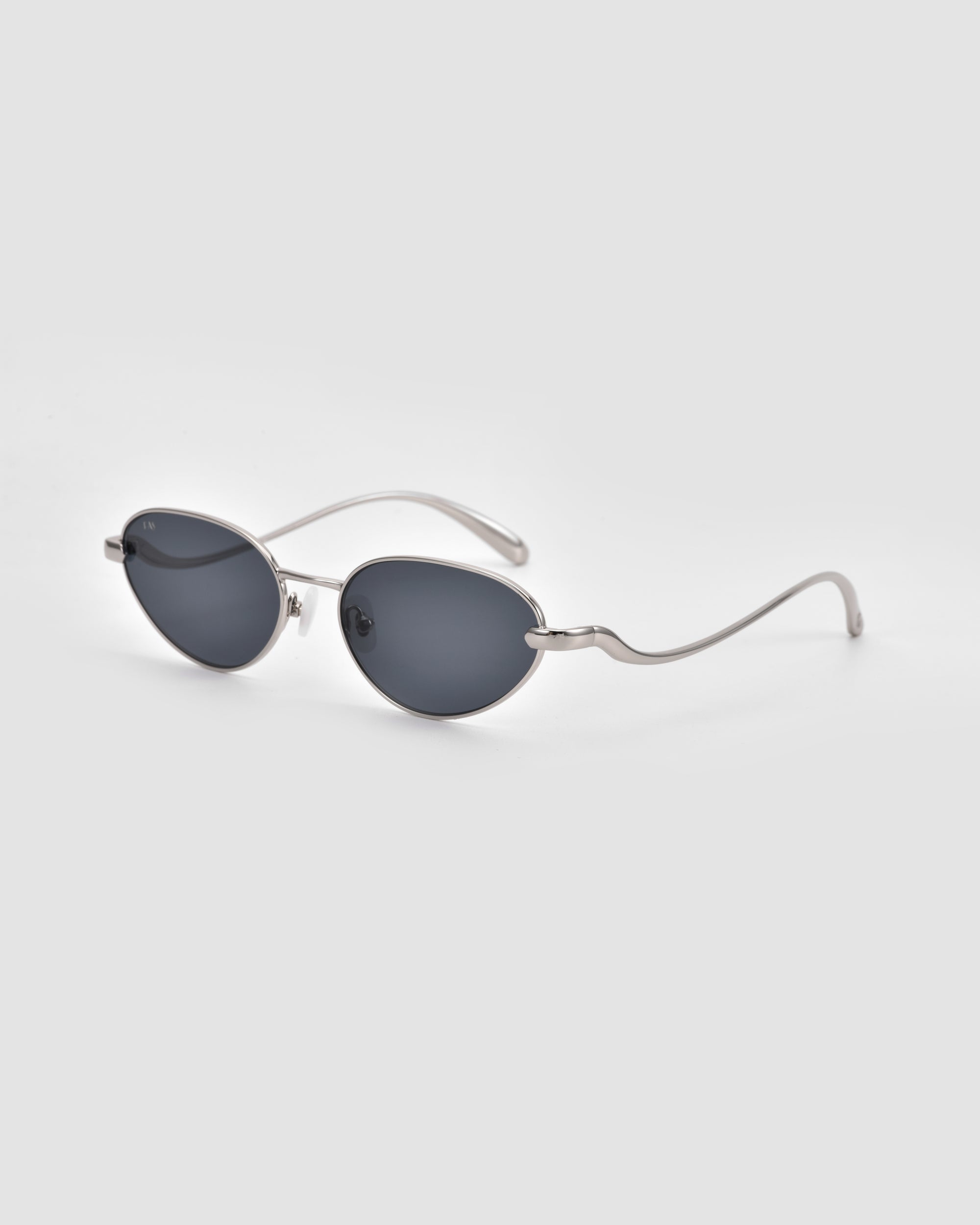 Rebirth sunglasses by For Art's Sake® feature oval dark lenses, thin silver metal frames, and uniquely wavy arms for a sculptural 3D effect—perfect futuristic style against a light gray backdrop.