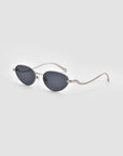 Rebirth sunglasses by For Art's Sake® feature oval dark lenses, thin silver metal frames, and uniquely wavy arms for a sculptural 3D effect—perfect futuristic style against a light gray backdrop.