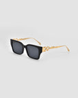 The Incomplete sunglasses by For Art's Sake® feature black boxy frames and gold geometric mosaic metal arms, shown on a light gray background.