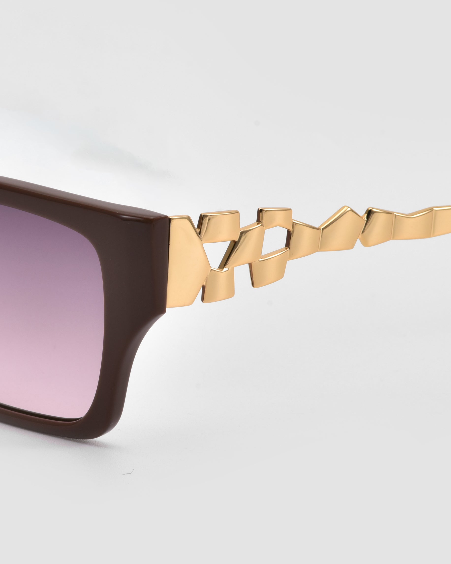 Close-up of For Art&#39;s Sake® Incomplete boxy square sunglasses featuring a brown acetate frame, purple-tinted lenses, and a unique gold geometric mosaic metal design on the temple arm against a plain light background.