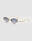 The Moment sunglasses by For Art's Sake® feature a thin metal frame and blue-tinted, cat-eye geometric lenses, shown against a plain light gray background.