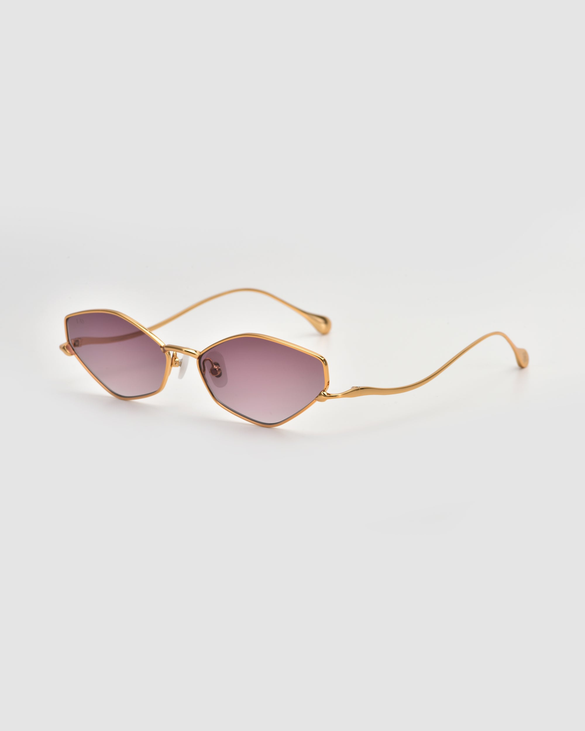 The Moment sunglasses by For Art's Sake® feature a gold-tone geometric frame with purple-tinted lenses, thin metal arms, and a sleek modern design, shown against a plain light background.
