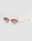 The Moment sunglasses by For Art's Sake® feature a gold-tone geometric frame with purple-tinted lenses, thin metal arms, and a sleek modern design, shown against a plain light background.