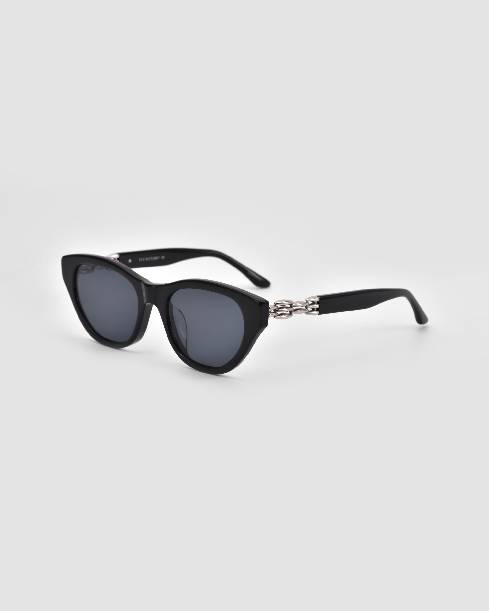 The Cuts by For Art's Sake®: black cat-eye sunglasses with dark lenses and bold 3D weaved metal chain-link temples, shown on a light gray background.