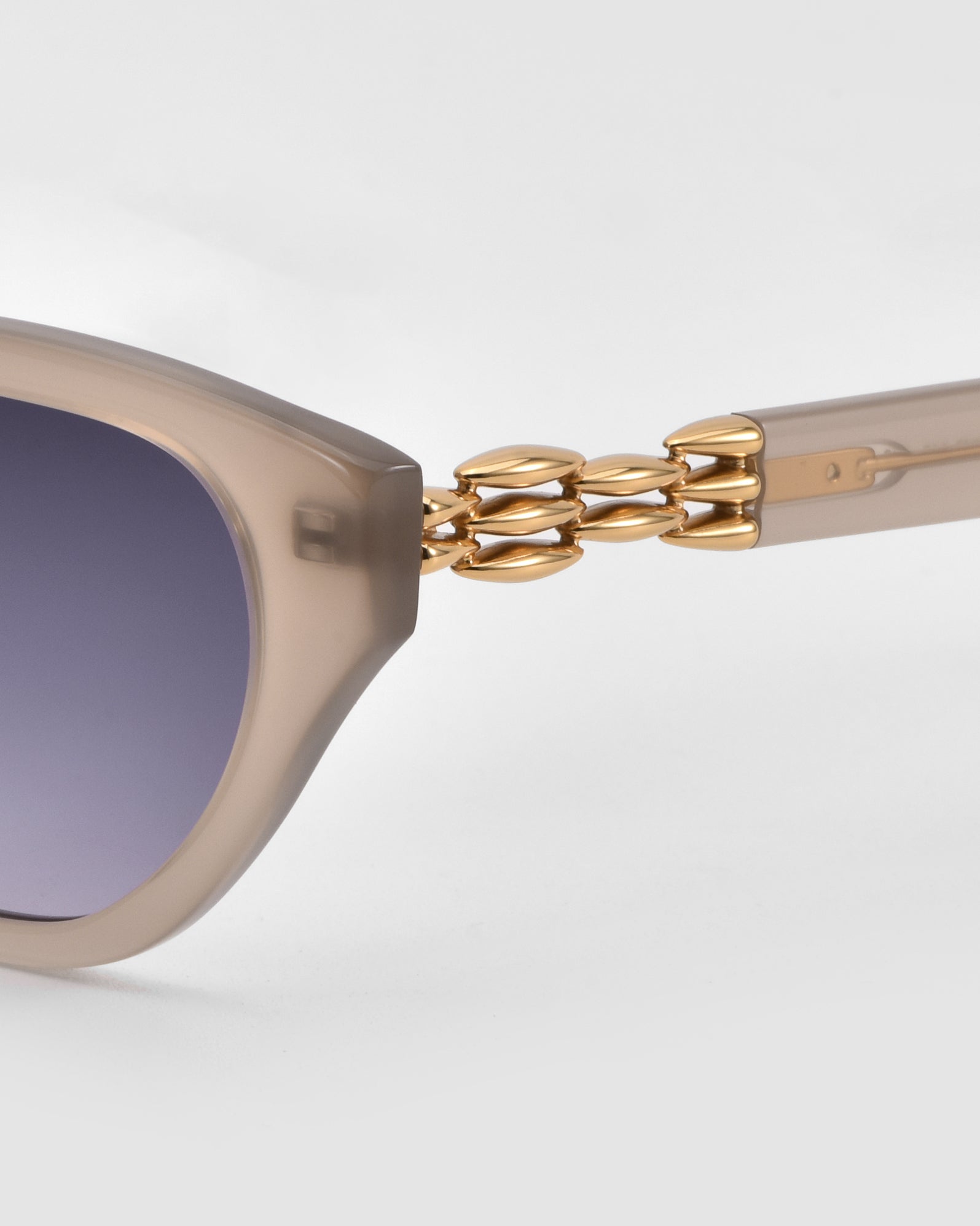 Close-up of The Cuts sunglasses by For Art&#39;s Sake®, showcasing a beige weaved metal frame, gradient dark lenses, and gold chain-link detailing on the temples against a plain light background.