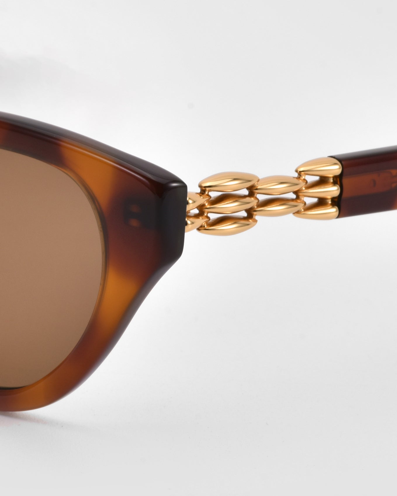 Close-up of The Cuts sunglasses by For Art&#39;s Sake®, featuring sculptural tortoiseshell frames and gold chain-link temple detailing, set against a light grey background.