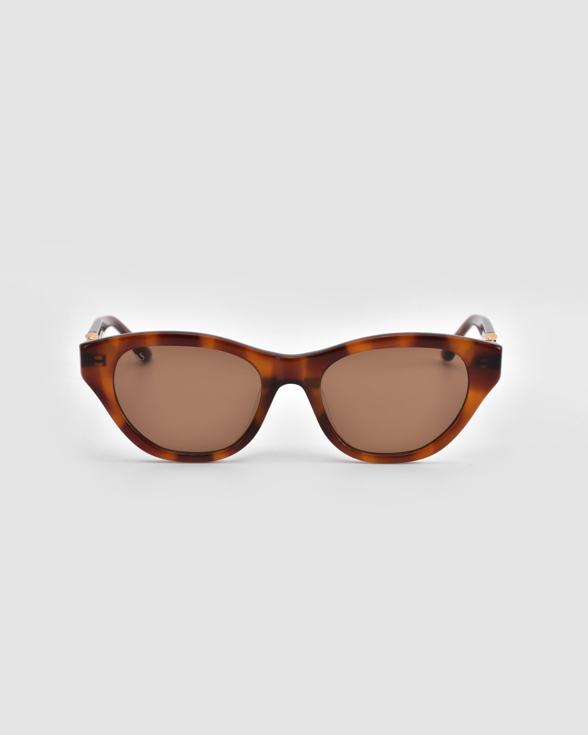 Front view of The Cuts oval tortoiseshell sunglasses by For Art’s Sake®, featuring brown-tinted lenses, displayed on a plain light gray background.
