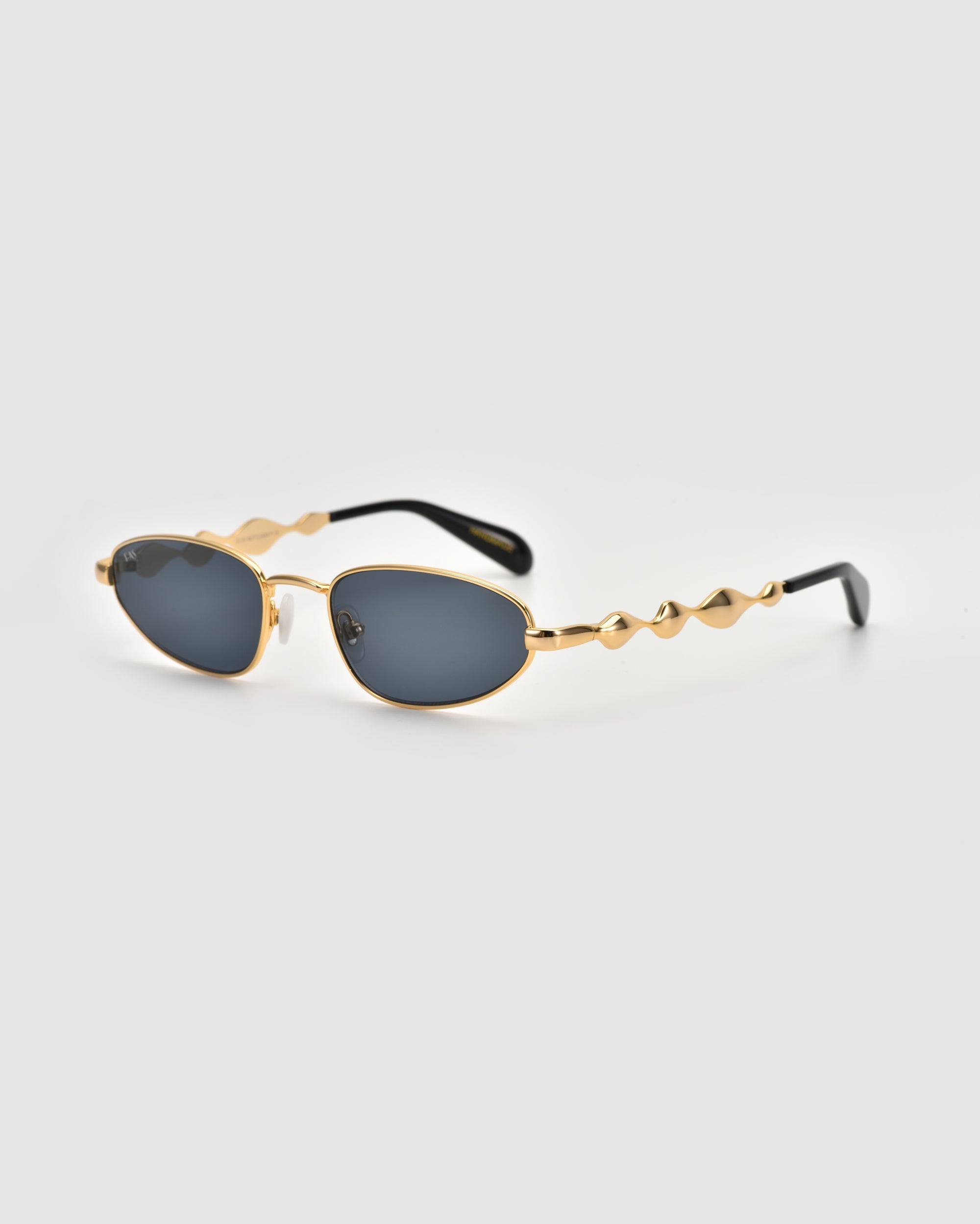 Droplets by For Art's Sake® are gold-framed, oval retro sunglasses with wavy temple arms, making a bold statement piece, shown on a light gray background.