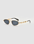 Droplets by For Art's Sake® are gold-framed, oval retro sunglasses with wavy temple arms, making a bold statement piece, shown on a light gray background.