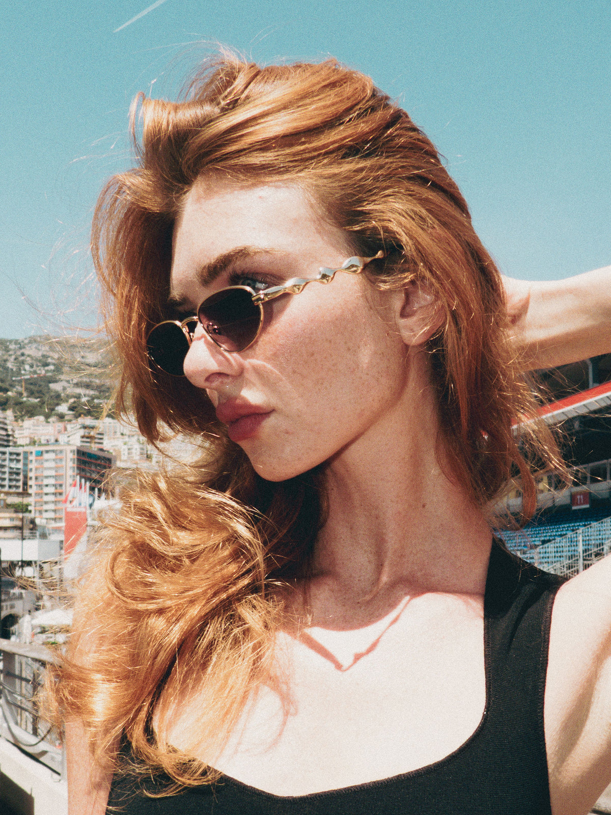 A woman wearing For Art's Sake Droplets champagne oval sunglasses outdoors against a city backdrop