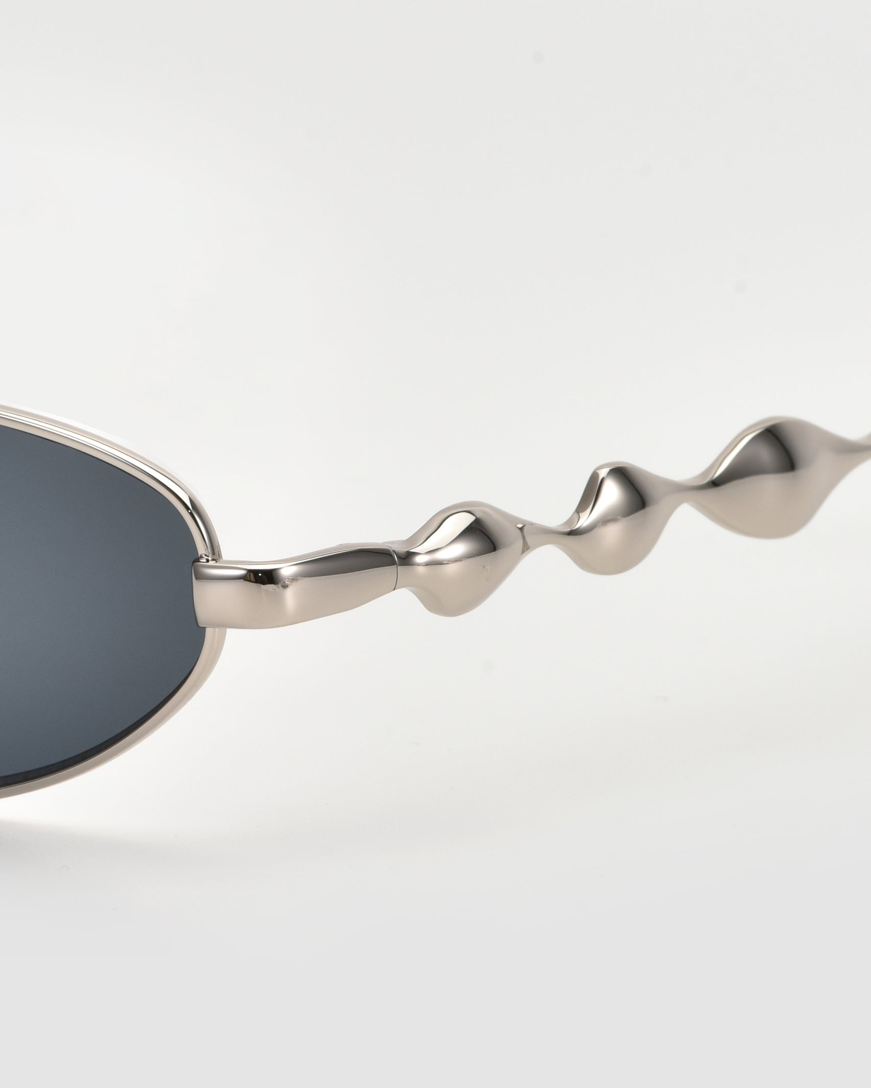 Close-up of For Art&#39;s Sake® Droplets: silver sunglasses with dark lenses and wavy, sculptural arms, ideal for bold, retro style lovers, set against a plain light gray background.