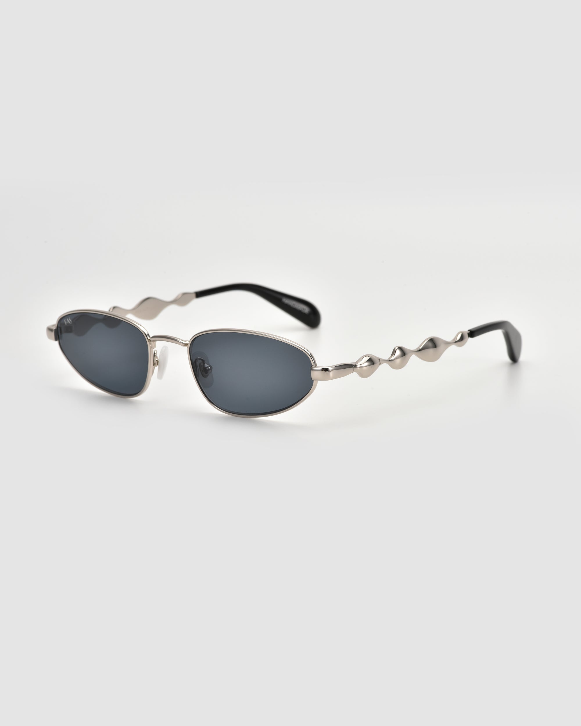 Droplets by For Art's Sake® are retro oval sunglasses with dark lenses, a sleek silver metal frame, wavy arms, and round accents, shown on a plain light background.