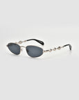 Droplets by For Art's Sake® are retro oval sunglasses with dark lenses, a sleek silver metal frame, wavy arms, and round accents, shown on a plain light background.