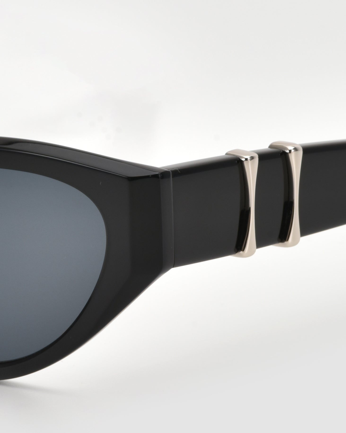 Close-up of Halo(S) sculptural sunglasses by For Art&#39;s Sake®, with an acetate frame, dark lenses, and two silver metallic accents near the hinge, shown against a plain light background.