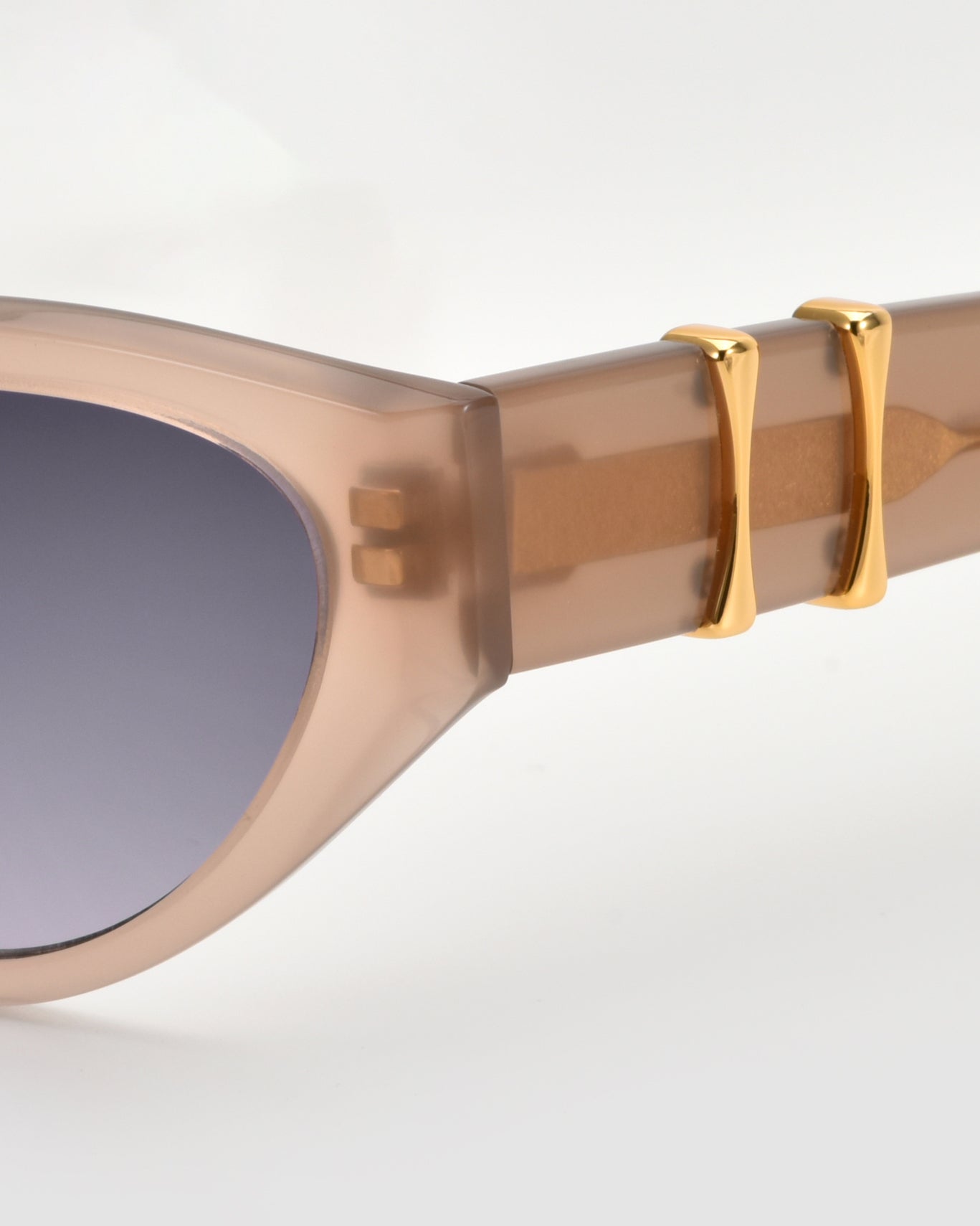 Close-up of For Art&#39;s Sake® Halo(S) sculptural sunglasses in taupe acetate with gradient lenses, featuring two gold accents on the arms near the frame.