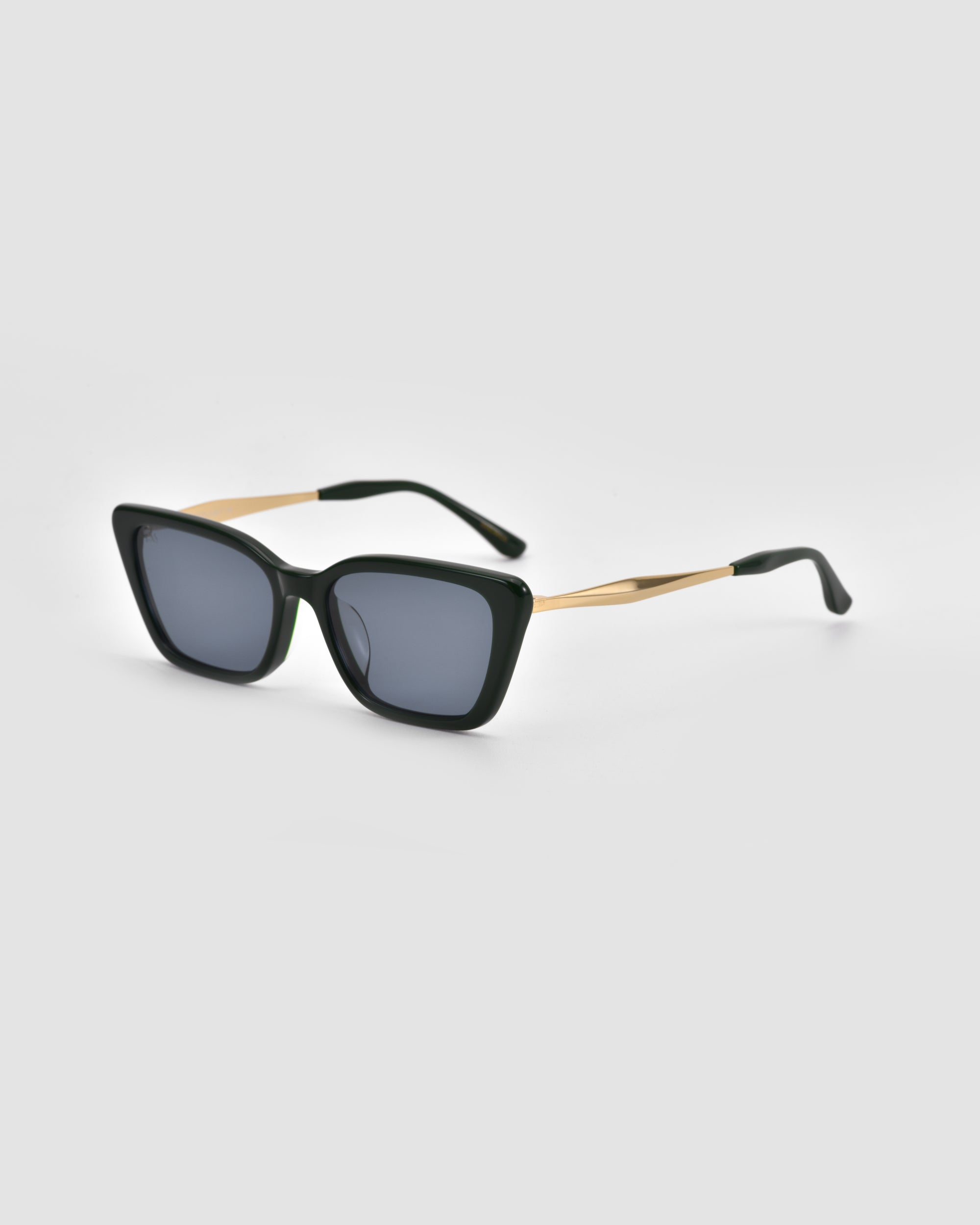 The Harmony(S) sunglasses by For Art's Sake® feature a sculptural rectangular black frame, dark lenses, and thin gold arms, showcased against a light grey background.