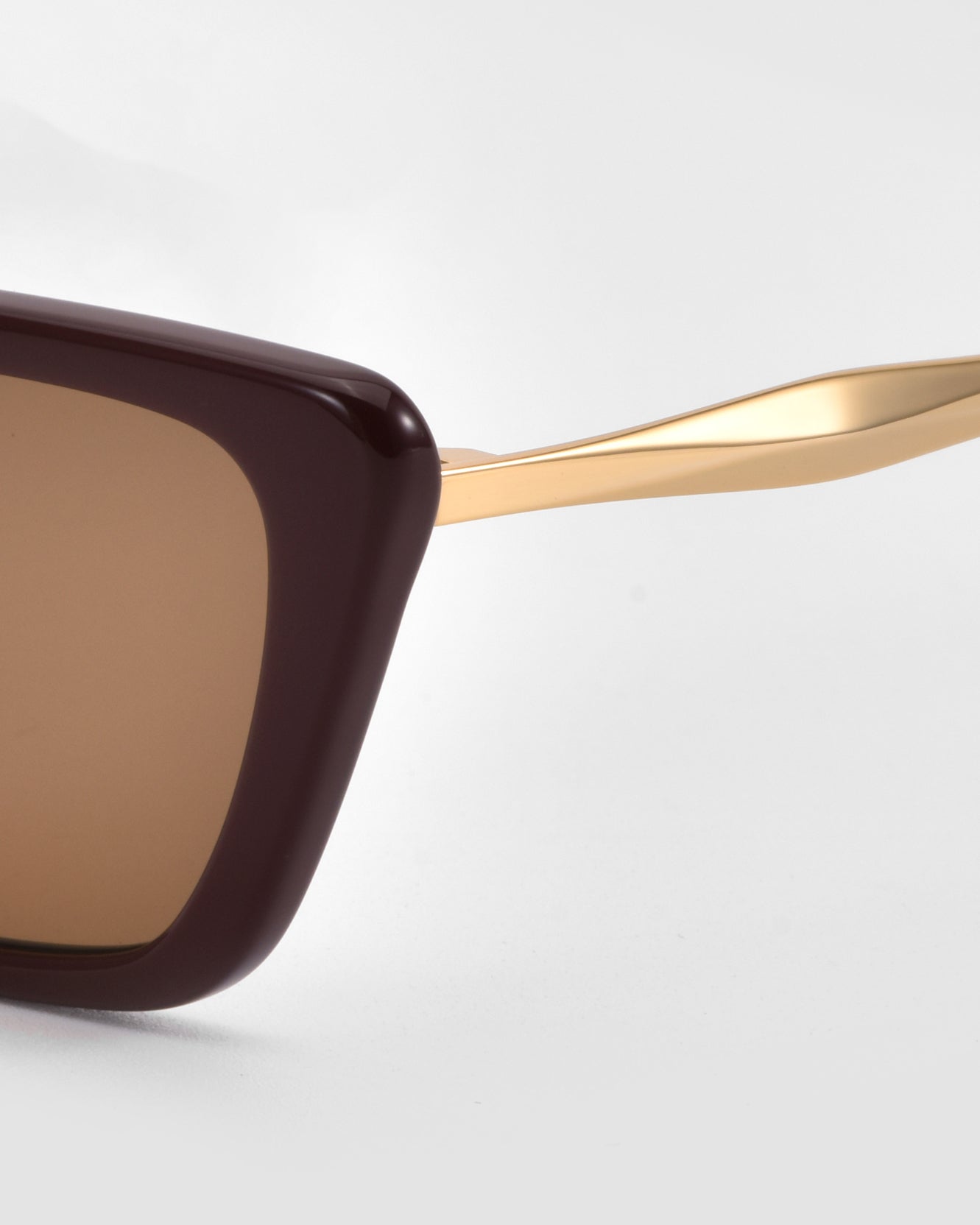 Close-up of Harmony(S) sunglasses by For Art&#39;s Sake®, showcasing a dark brown rectangular sculptural frame with gold metal arms against a plain light gray background.