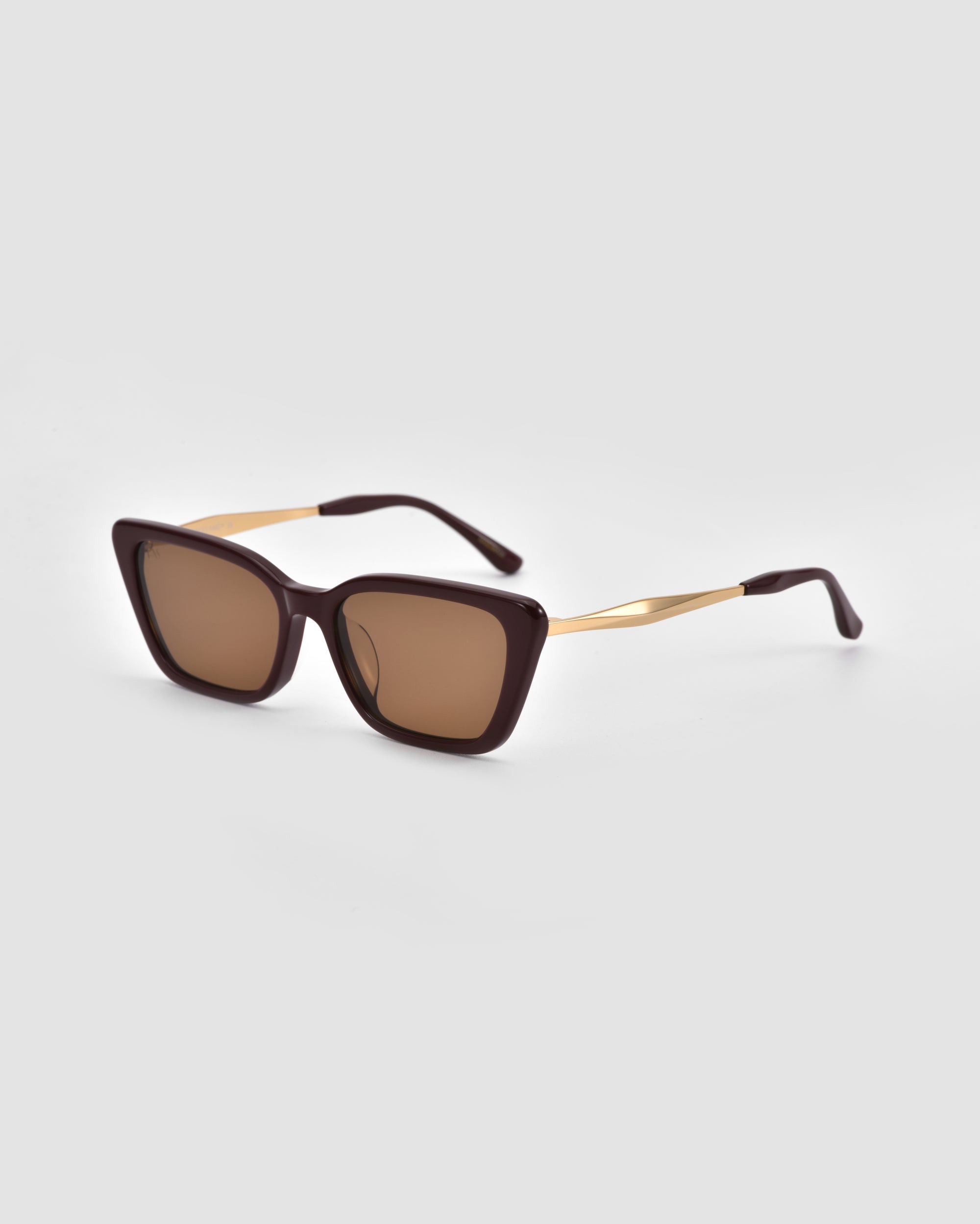 The Harmony(S) square minimal sunglasses by For Art's Sake® feature dark brown frames, gold arms, and brown tinted lenses, shown on a light gray background.