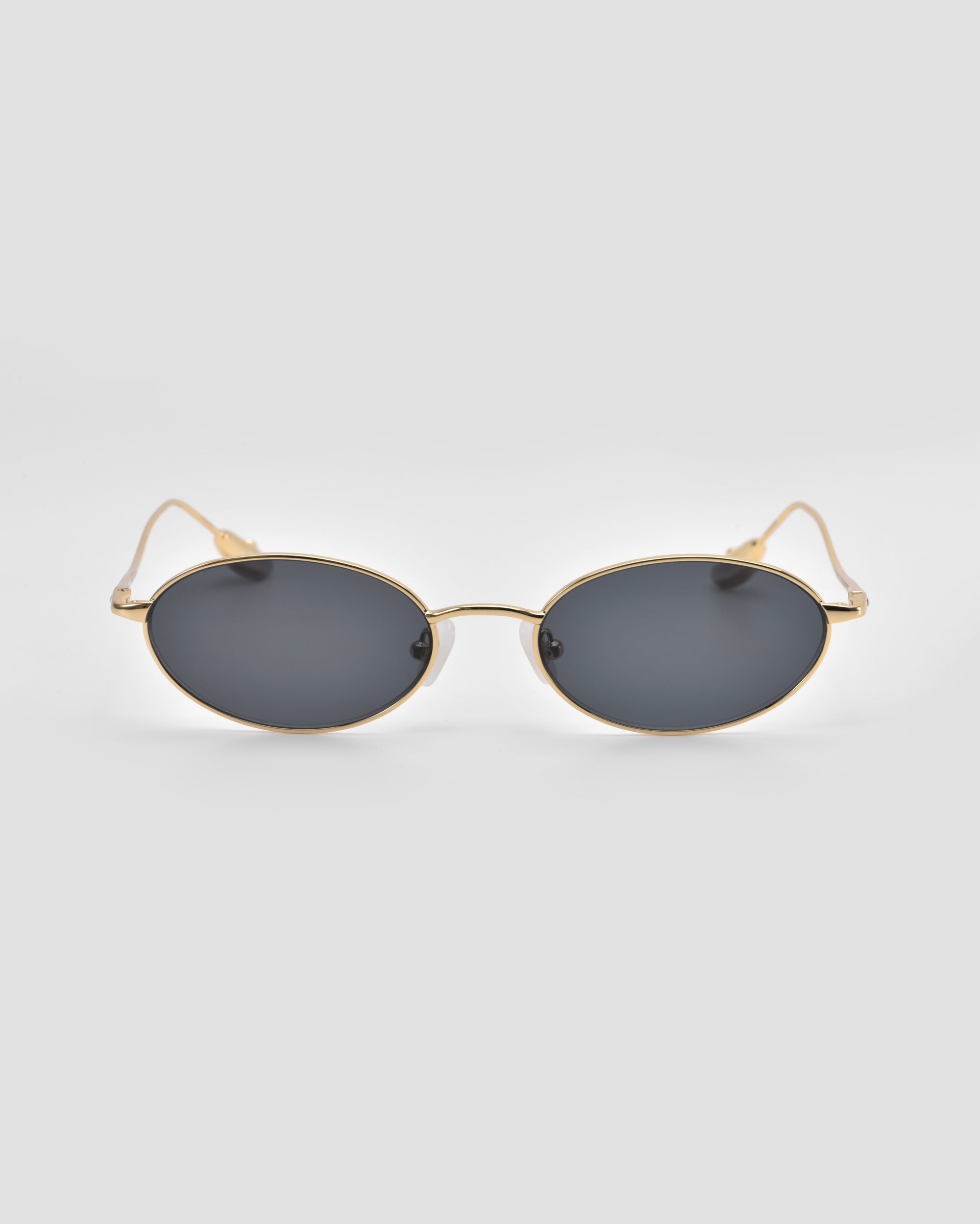 For Art's Sake® Calla I: Modern oval metal eyeglasses with dark lenses and thin gold frames offer lightweight, sculptural style, displayed facing forward on a light gray background.