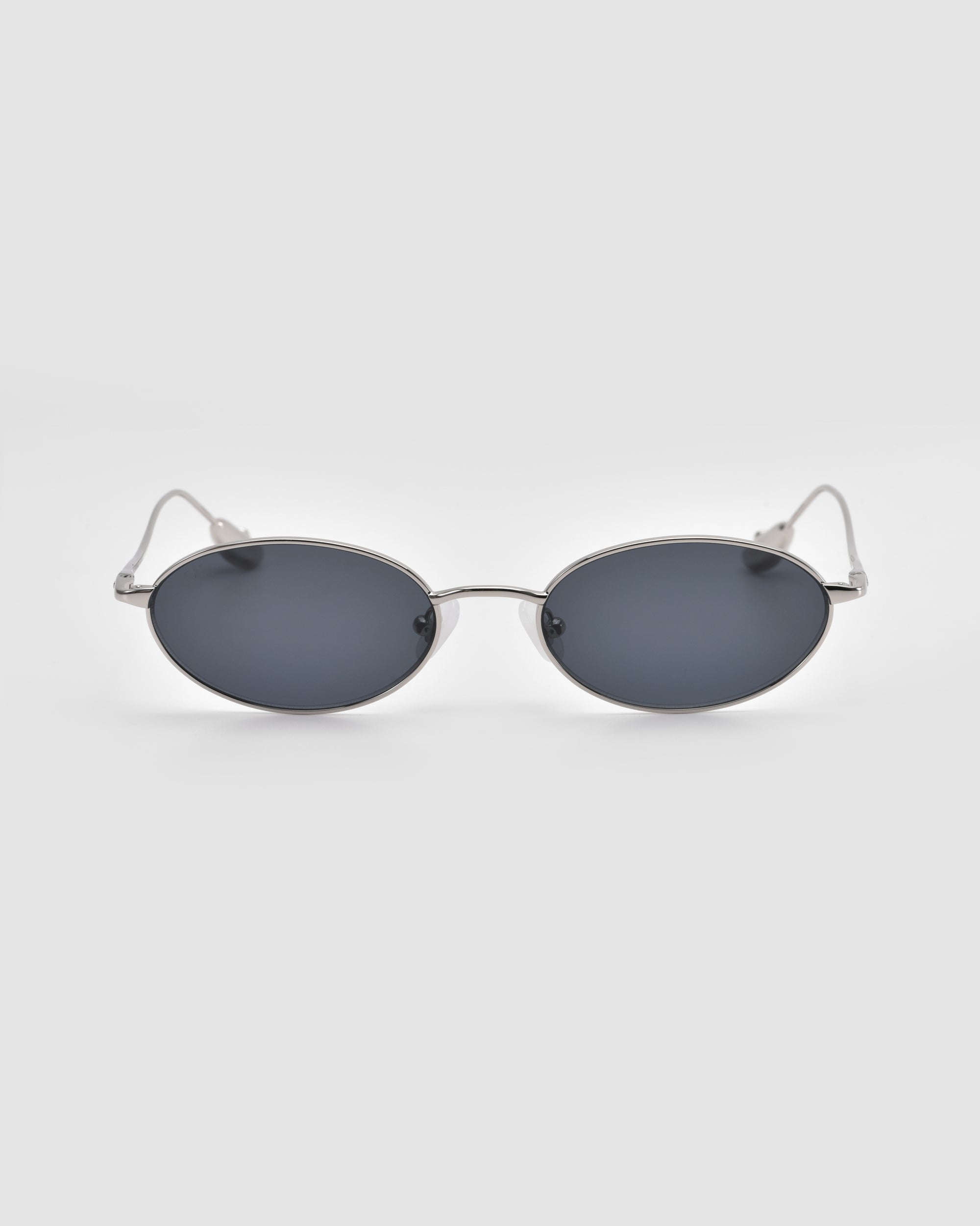 The For Art's Sake® Calla I sunglasses feature a sleek, modern oval metal silhouette with dark lenses and thin silver frames, shown against a plain light gray background.
