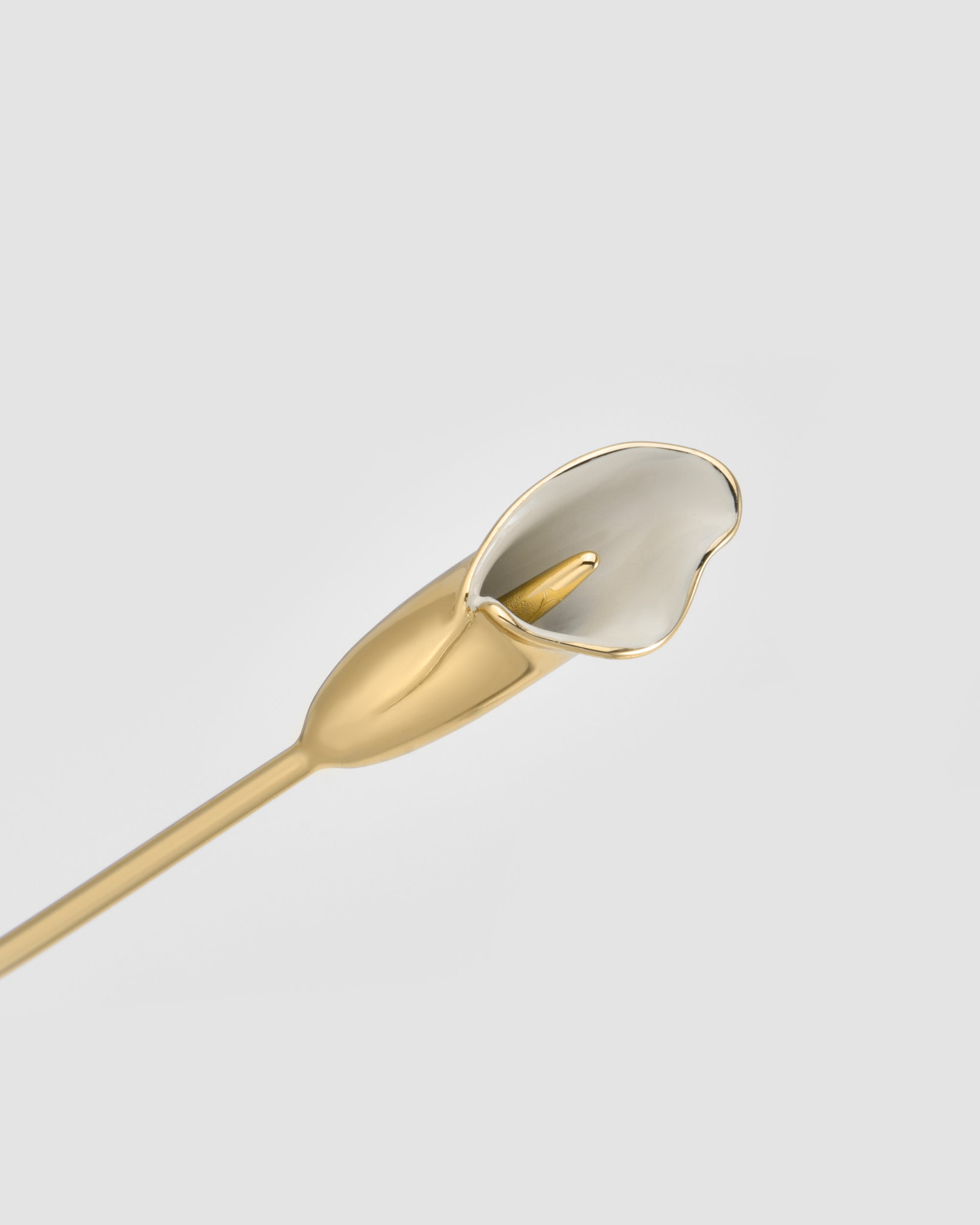 A gold and white metallic flower sculpture, reminiscent of a calla lily, sits on a thin gold stem against a light gray background—an elegant nod to For Art's Sake® Calla II eyewear and its lightweight sculptural design.