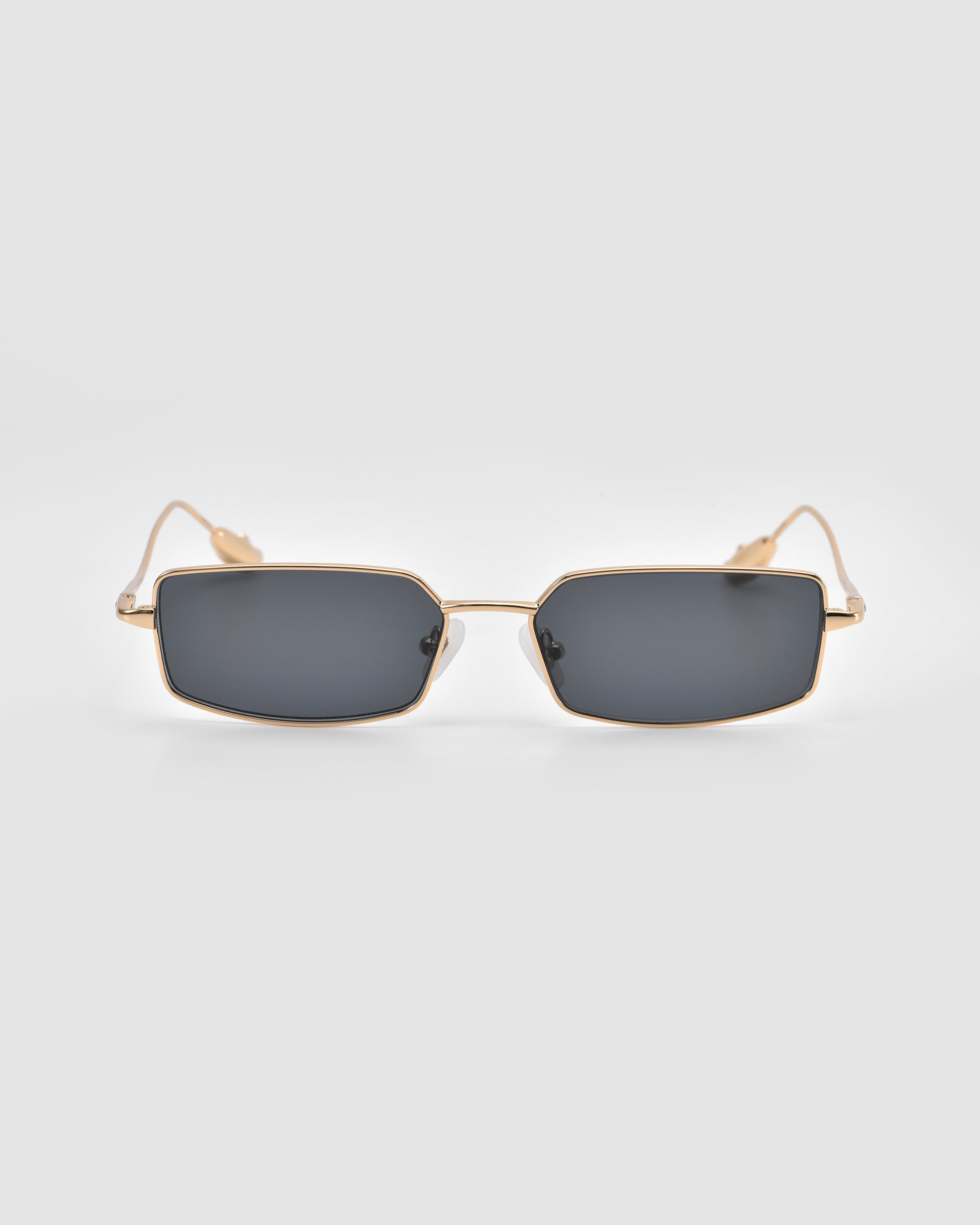 Calla II by For Art's Sake®: Rectangular sunglasses with dark lenses and slim gold frames, displayed front-on against a light gray background—a sleek pick for lightweight, sculptural eyewear lovers.