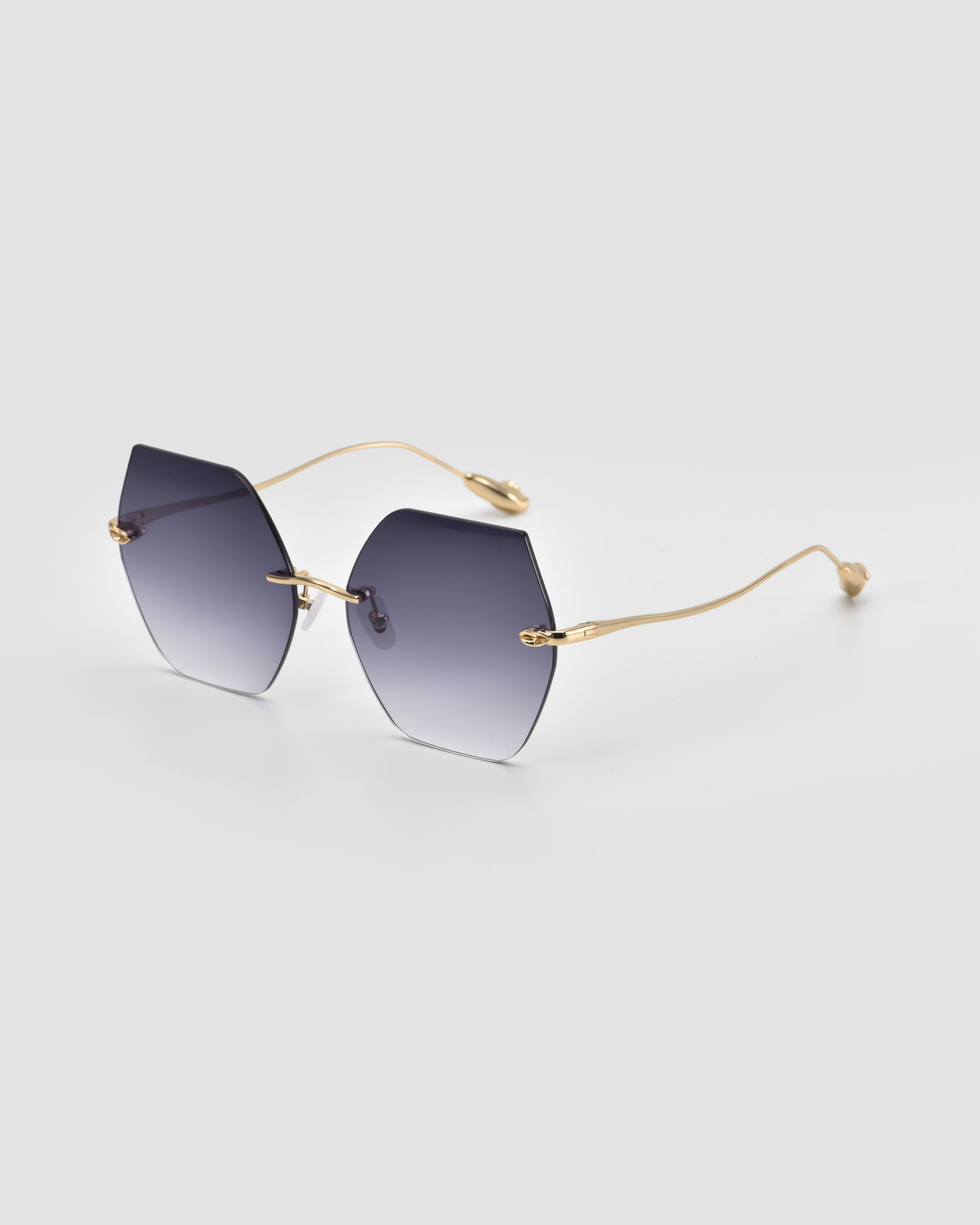 The Georgia by For Art's Sake® features hexagonal oversized frameless sunglasses with gradient lenses and slim gold metal temples, displayed against a light gray background.