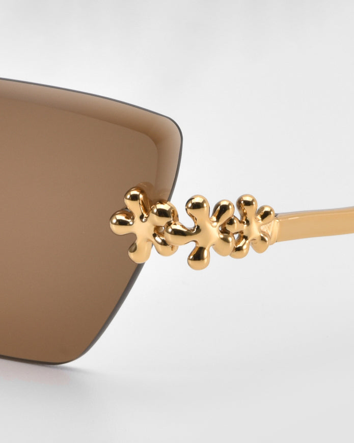 Close-up of the Florist sunglasses by For Art’s Sake®, featuring brown frames and sculpted floral accents on the arms, set against a plain light background.