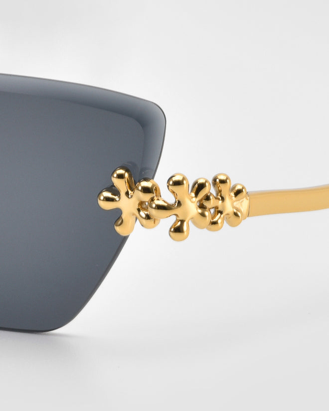 Close-up of For Art’s Sake® Florist sunglasses in black, showcasing gold sculpted floral accents on the hinges and arms, set against a plain light background.