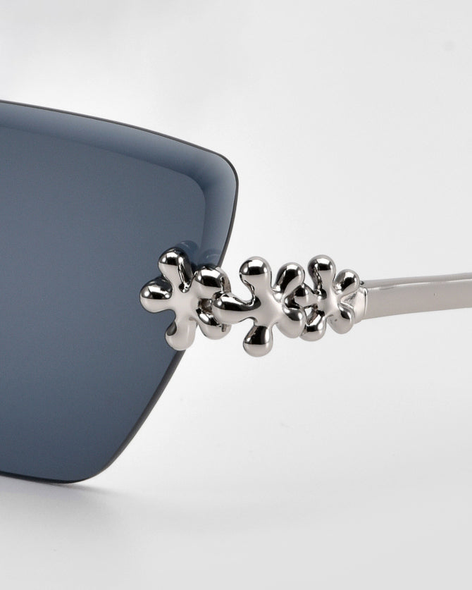 Close-up of For Art's Sake® Florist sunglasses with dark blue lenses and a silver metallic frame. Sculpted floral accents on the arm near the lens add an elegant decorative touch.