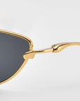 Close-up of For Art’s Sake® Lake cat-eye sunglasses with a gold metal frame, black lenses, and sculpted temples and hinge detail shown against a light gray background.