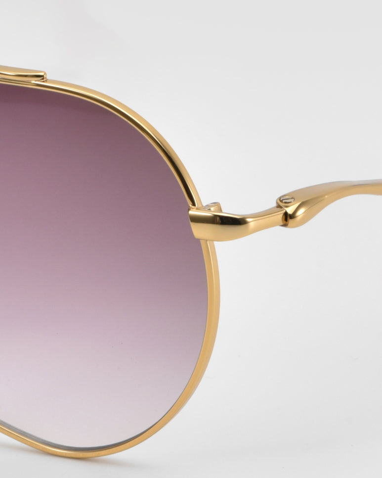 Close-up of the right lens and gold metal frame of For Art’s Sake® Lines oversized aviator sunglasses with a gradient purple tint and sculpted temples, set against a plain light background.
