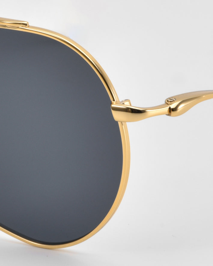 Close-up side view of For Art’s Sake® Lines oversized aviator sunglasses with gold metal frames, sculpted temples, and dark tinted lenses set against a plain light background.