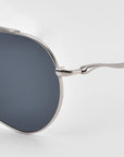 Close-up of For Art's Sake® Lines oversized aviator sunglasses with dark round lenses, showcasing the hinge and sculpted temples on a slim silver frame, set against a plain white background.
