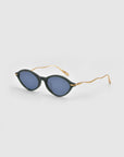 For Art's Sake® Totto black round sunglasses with blue lenses and gold wavy sculpted temples, made from acetate and metal, shown on a plain light gray background.