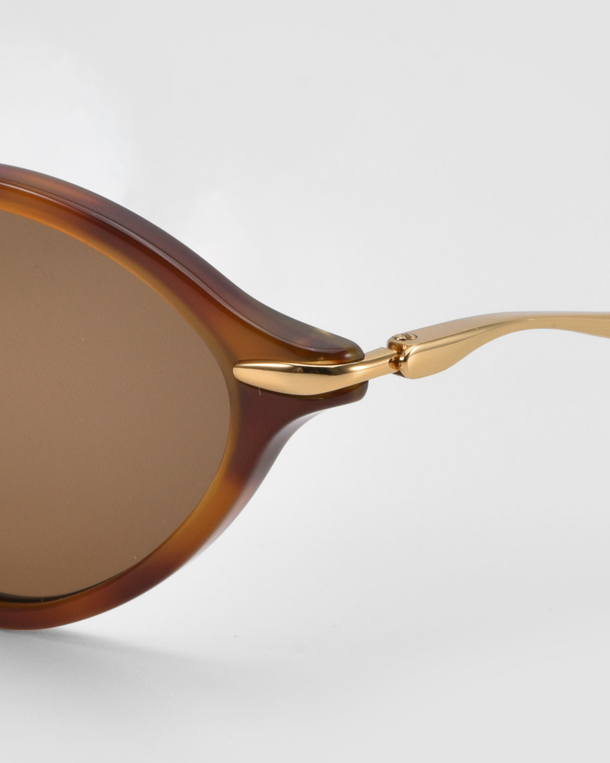 Close-up of For Art's Sake® Totto sunglasses with brown-tinted lenses, a brown frame, sculpted acetate and metal temples, plus gold metallic hinge and temple arm against a plain light background.