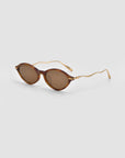 For Art's Sake® Totto sunglasses feature round brown frames, tinted lenses, and thin wavy gold metal sculpted temples, shown on a light gray background.