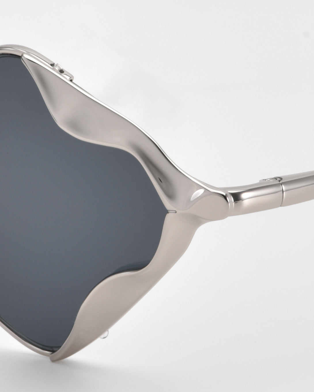 Close-up of For Art's Sake® Leaf I sunglasses featuring dark, diamond-shaped lenses and a sculptural silver wavy frame, showcased against a white background.