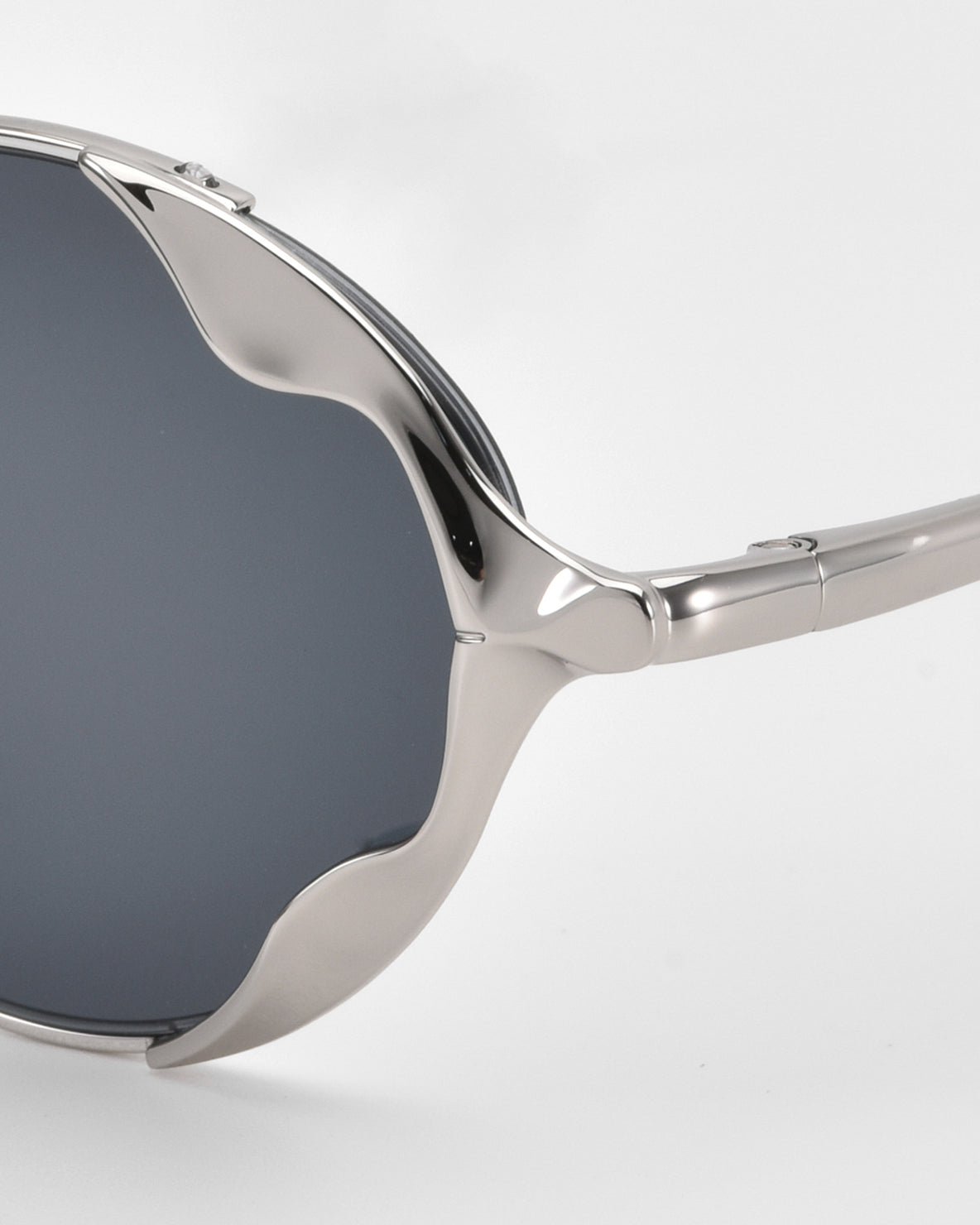 A close-up of For Art's Sake® Leaf II sculptural sunglasses featuring dark lenses and a shiny, wavy silver metal frame, displayed against a plain white background.