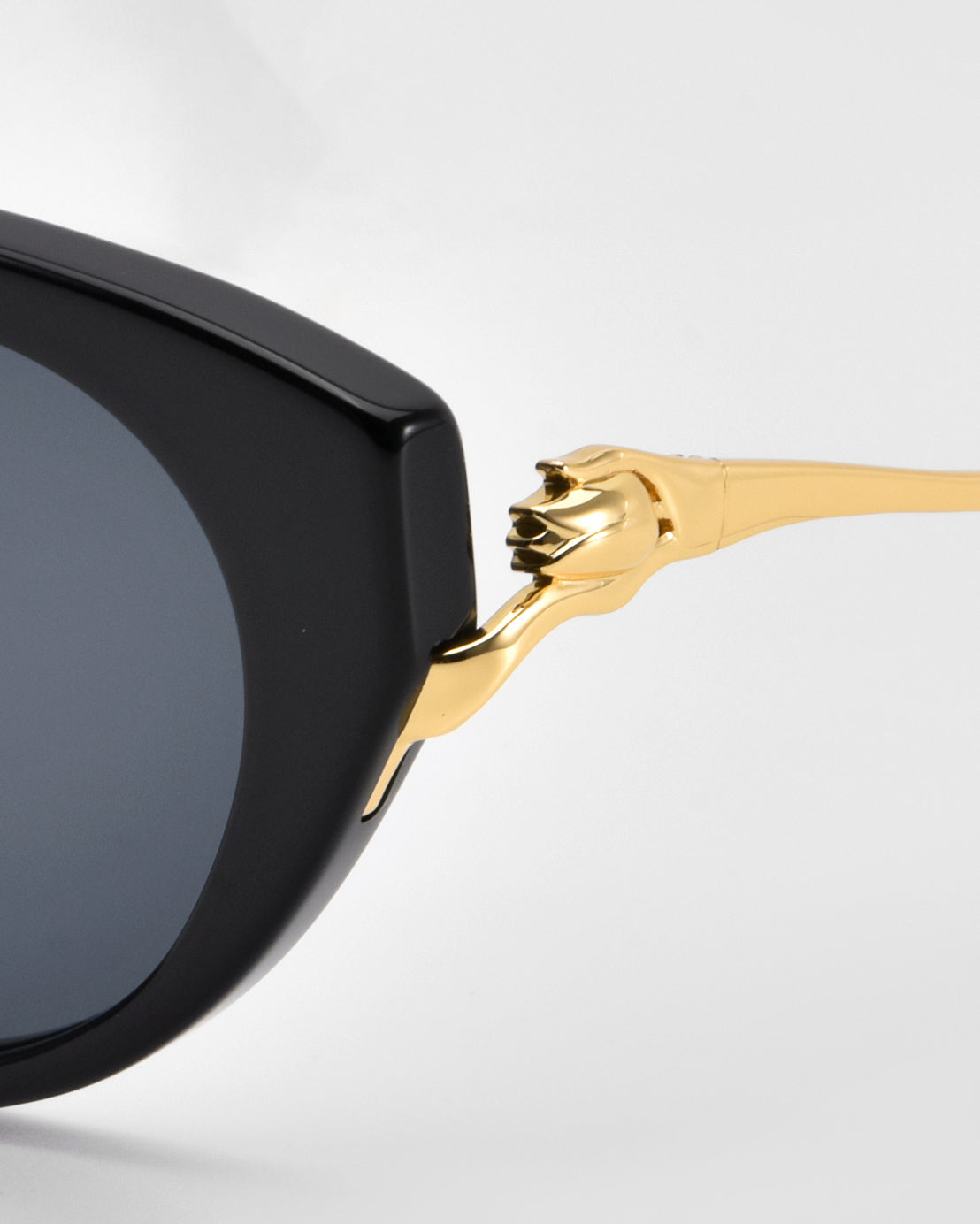 Close-up of For Art’s Sake® Tulip I sunglasses in bold acetate with dark lenses, featuring a gold temple shaped like a panther’s head and paw gripping the frame. Set against a plain light gray background for an elegant look.