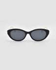 The Tulip I sunglasses by For Art's Sake® feature a bold black cat-eye acetate front, dark lenses, gold arms, and sculpted tulip details, shown on a plain light gray background.