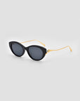 For Art's Sake® Tulip I cat-eye sunglasses with dark lenses and gold metal temples, sculpturally designed, shown on a light gray background.