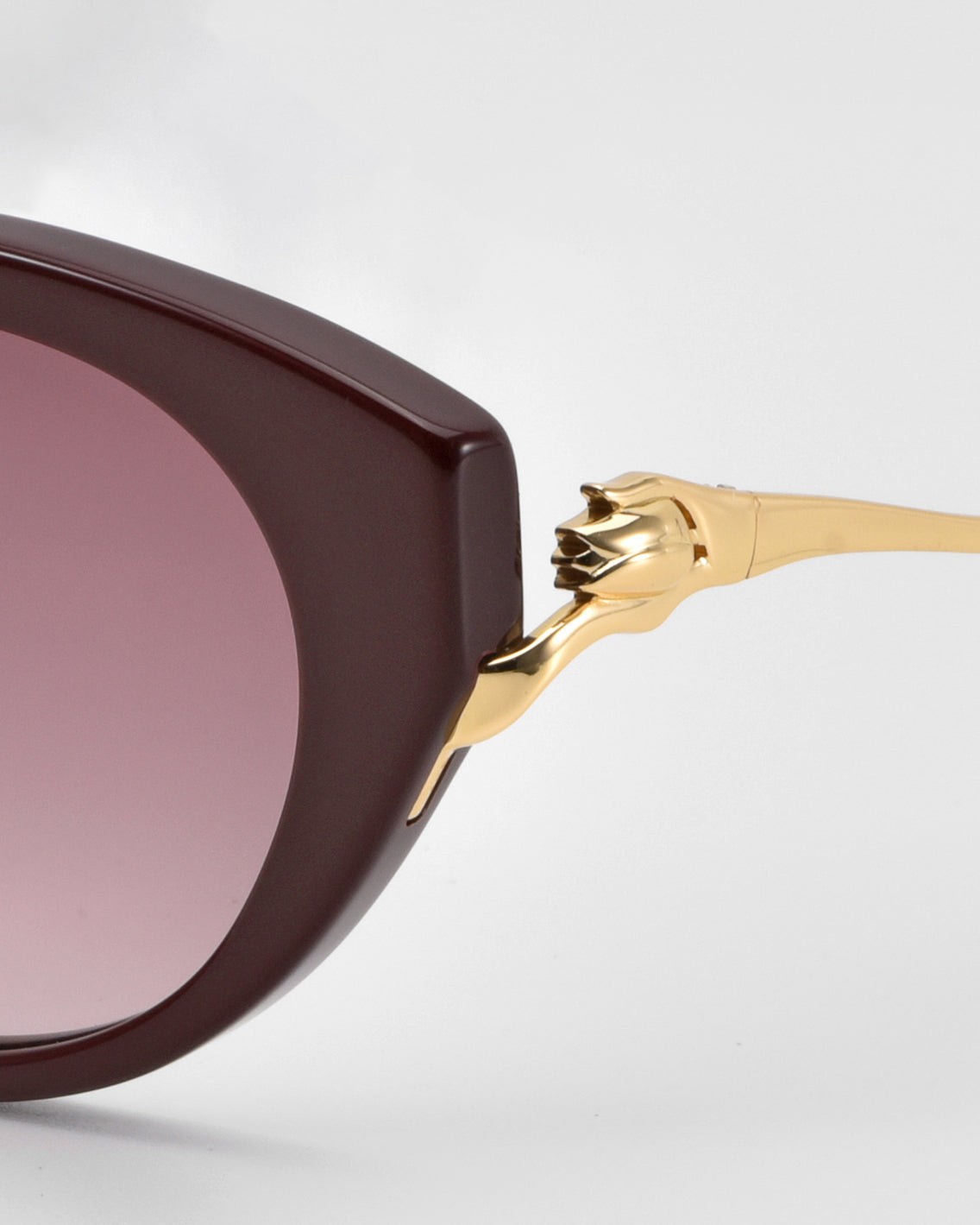 Close-up of For Art's Sake® Tulip I sunglasses, featuring bold maroon acetate frames, gradient pink lenses, and gold temples with a sculptural claw detail gripping the frame.