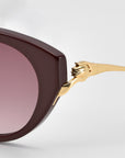 Close-up of For Art's Sake® Tulip I sunglasses, featuring bold maroon acetate frames, gradient pink lenses, and gold temples with a sculptural claw detail gripping the frame.