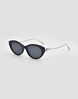 For Art's Sake® Tulip I features black cat-eye sunglasses with a sculptural design, dark lenses, and thin silver metal arms, displayed on a light gray background.
