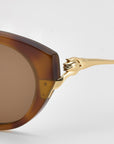 Close-up of Tulip I sunglasses by For Art's Sake®—bold acetate in brown with gold metal temples and a sculptural lion head at the hinge, shown against a white background to highlight their striking design.