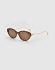 For Art's Sake® Tulip I sunglasses feature a bold brown cat-eye acetate front, gold metal arms, and tinted brown lenses in a sleek, modern design. Shown on a plain light gray background.