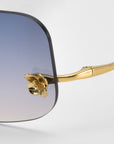 Close-up of For Art's Sake® Magnolia sunglasses, showcasing a gold frame, gradient blue-to-clear lenses, and a signature decorative gold flower detail at the hinge.