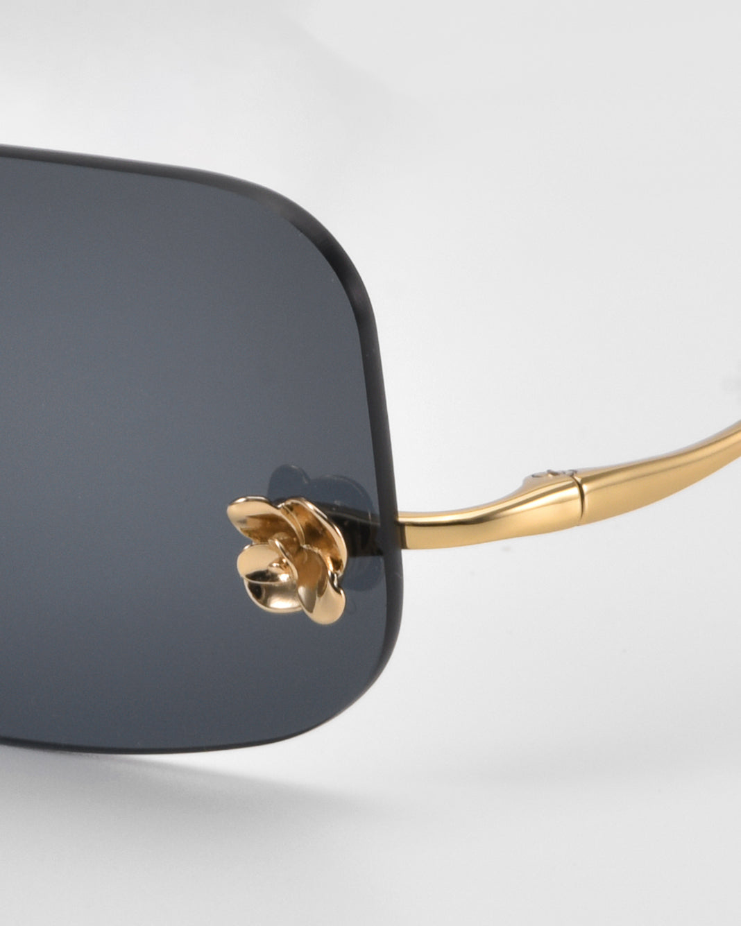 Close-up of For Art's Sake® Magnolia sunglasses, featuring a dark rectangular lens, gold metal frame, gold nose pad, and curved gold temple arm against a plain light background.